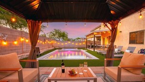 An outdoor patio with a pool, lounge chairs, and a table with a bottle and glasses. - Spacious 5 BD Home w/Theater, Billiard, and More! (North Las Vegas)