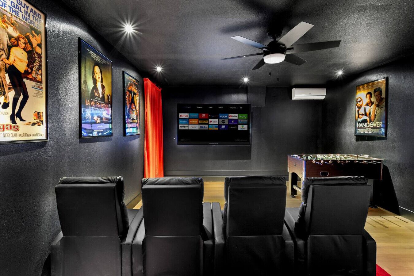 A room with black leather chairs, a foosball table, a ceiling fan, and movie posters on the walls.