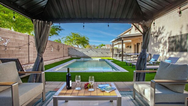 An outdoor patio with a pool, seating, and a table with a bottle and glasses. - Spacious 5 BD Home w/Theater, Billiard, and More! (North Las Vegas)