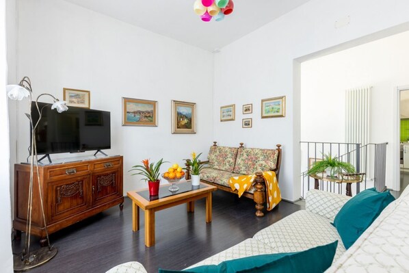 A living room with a sofa, a wooden cabinet, a television, and a floral-patterned sofa.