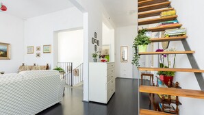 Een moderne slaapkamer met een bed, een dressoir, een trap met boekenkasten en een gang naar een andere kamer.