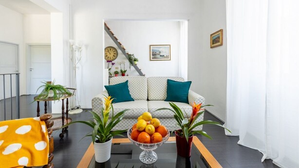Een woonkamer met een bank, een bijzettafeltje met fruit en een trap.