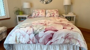 A bedroom with a floral bedspread, two bedside lamps, a round wall art piece, and a potted plant. - Beautiful Queen Suite near Castle, City & Beach (Victoria)