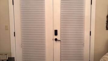 A room with a double door closet, a bed with floral bedding, and a small black appliance on the floor.