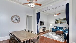 A dining area with a wooden table and chairs, a ceiling fan, and a television in the background. - The Tchoup Shop (New Orleans)