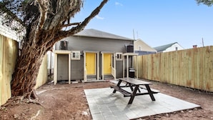 A backyard with a picnic table, a wooden fence, and a tree. - The Tchoup Shop (New Orleans)
