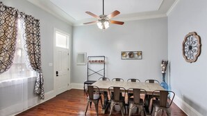 A dining room with a wooden table, metal chairs, a ceiling fan, and a decorative wall piece. - The Tchoup Shop (New Orleans)