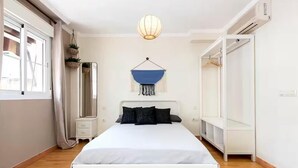 Une chambre avec un lit blanc, une chaise bleue suspendue, une armoire et un miroir.