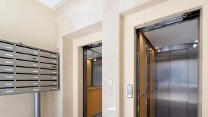 Un ascenseur aux finitions métalliques, un espace pour le dépôt du courrier doté de plusieurs compartiments et un sol recouvert de carreaux de marbre.