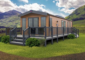 A modern cabin with a deck, large windows, and a mountainous backdrop.