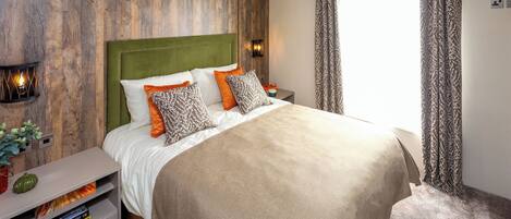 Une chambre à coucher avec un grand lit, une table de chevet avec une lampe, un luminaire fixé au mur et une fenêtre avec des rideaux.