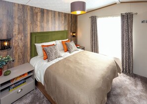 Een slaapkamer met een groot bed, een nachtkastje met een lamp, een wandlamp en een raam met gordijnen.