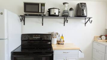 Eine Küche mit Herd, Mikrowelle und Kaffeemaschine auf einem Regal, einem Mixer und einer Holzausziehtafel mit Geschirr.