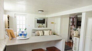 Una cocina moderna con una isla central, taburetes de bar, un televisor de pantalla plana y un comedor con sofá y mesa.
