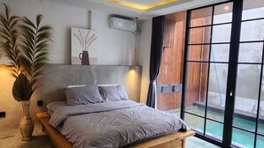 A modern bedroom with a large bed, a potted plant, and a view of a swimming pool through a sliding glass door. - Sienna House Kerobokan (Kerobokan)