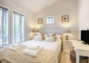 Een slaapkamer met een bed, nachtkastjes, lampen, een bureau en een televisie.