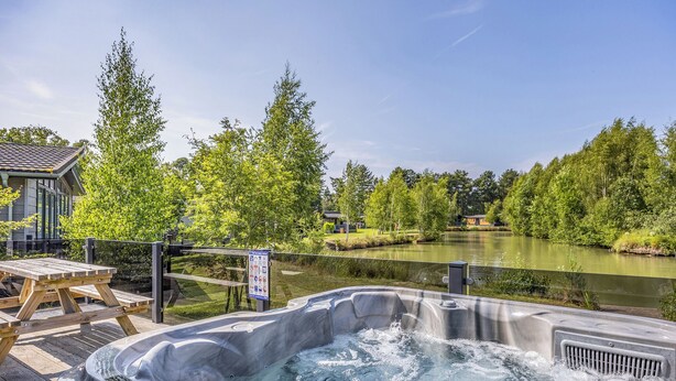 A hot tub with a view of a lake and trees. - Luxury new Lakeside lodge with spacious and open plan living and kitchen area. (Woodhall Spa)
