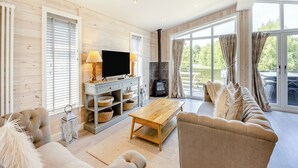 A modern living room with a flat-screen TV, wooden flooring, a fireplace, a sofa, and large windows. - Luxury new Lakeside lodge with spacious and open plan living and kitchen area. (Woodhall Spa)