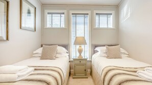 Een slaapkamer met twee bedden, een nachtkastje met een lamp en een raam met jaloezieën.