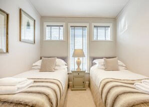 Une chambre avec deux lits, une table de chevet avec une lampe et une fenêtre avec des stores.