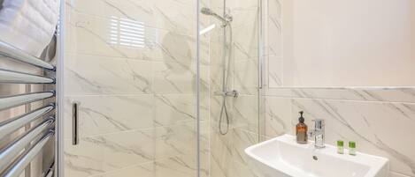 A modern bathroom with a glass shower enclosure, a white sink, and a towel rack.