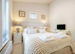 A neatly arranged bedroom with a bed, two bedside tables with lamps, a TV, and framed artwork on the wall.