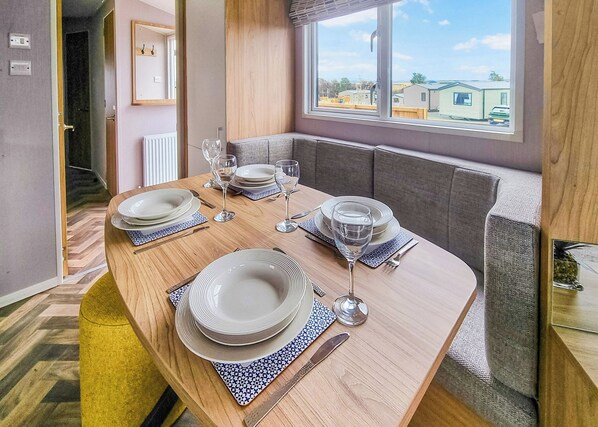 A dining table set with plates, glasses, and cutlery, a window with a view of houses, and a door leading to another room.