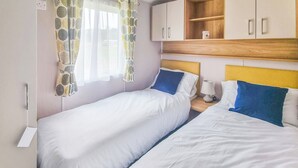 Une chambre avec deux lits, une fenêtre avec des rideaux à motifs, une table de chevet avec une lampe et des armoires en bois au-dessus des lits.