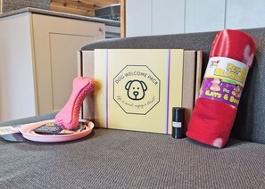 A dog welcome pack, a pink bone toy, and a red blanket on a couch.