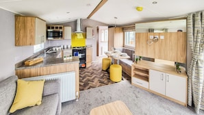 Une cuisine compacte dotée d’un îlot central, un coin repas avec une table et des chaises, et un espace salon confortable avec des coussins.