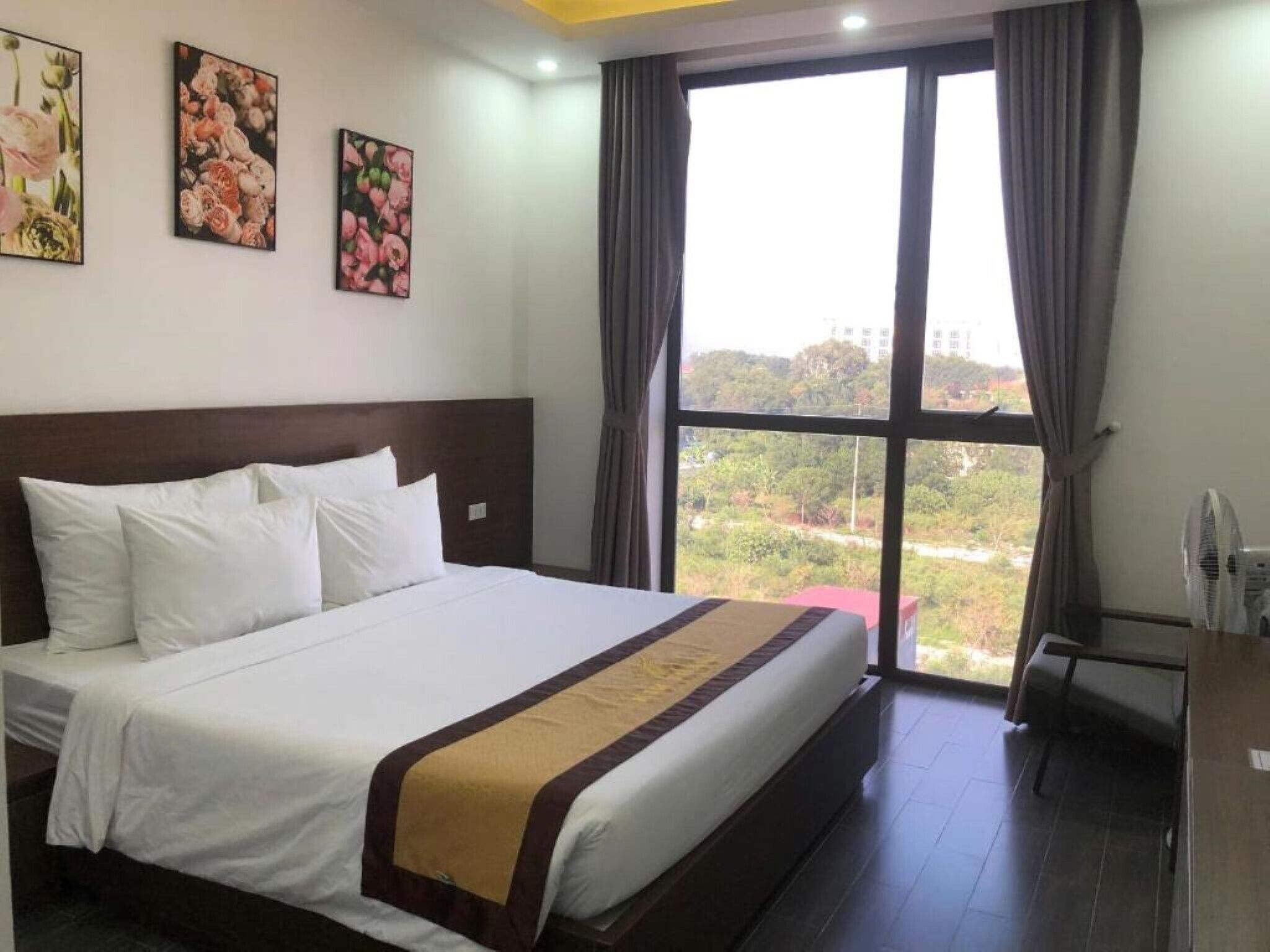 Habitación de hotel con una cama grande, vista por la ventana y un ventilador a la derecha.