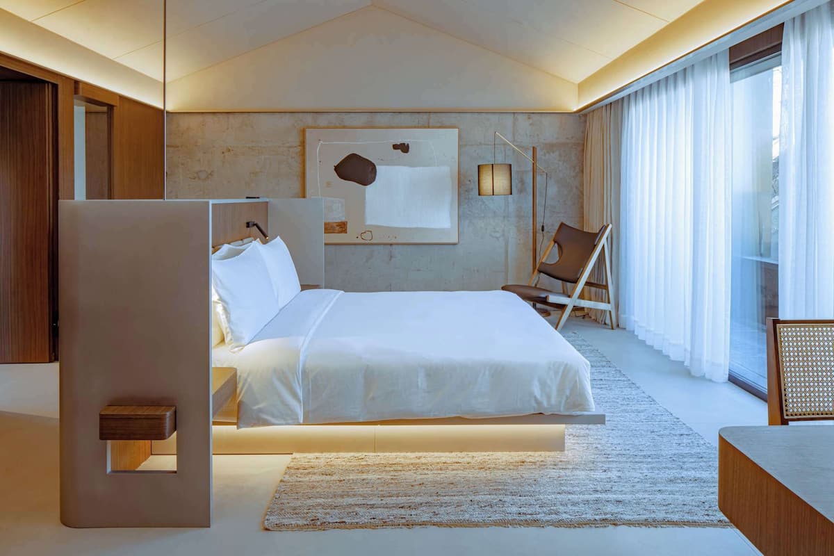 Un dormitorio moderno con una cama grande, una mesita de noche, una silla y una obra de arte en la pared.