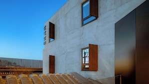 Un bâtiment moderne doté d’une façade en béton, de grandes fenêtres et d’un escalier apparent menant à un étage supérieur.