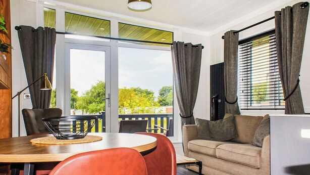 Een moderne woonkamer met een eettafel, rode stoelen, een beige bank en een balkon met gordijnen.
