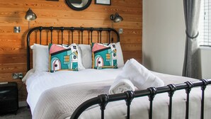 Een netjes opgemaakt bed met een witte dekbedovertrek en kussens, een ronde spiegel aan de muur en ingelijste motiverende citaten.