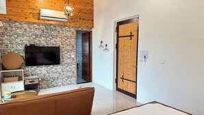 Une chambre moderne avec un mur en pierre, une porte en bois, un lit, une télévision et un coin salon avec un panier et une télécommande.