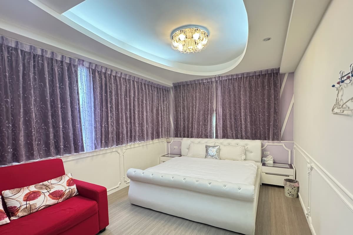 A modern bedroom with a large bed, a red sofa, and a chandelier.