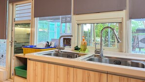 Une cuisine avec deux éviers, des meubles en bois, une fenêtre avec des stores et un bac de rangement vert.
