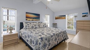 A bedroom with a bed, a ceiling fan, and artwork on the walls.