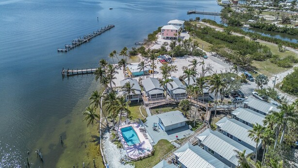 An aerial view of a coastal property with a swimming pool, multiple buildings, and a pier extending into the water.