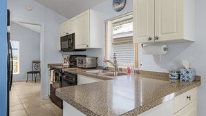 A kitchen with white cabinets, a granite countertop, a microwave, a toaster, and a window with blinds.