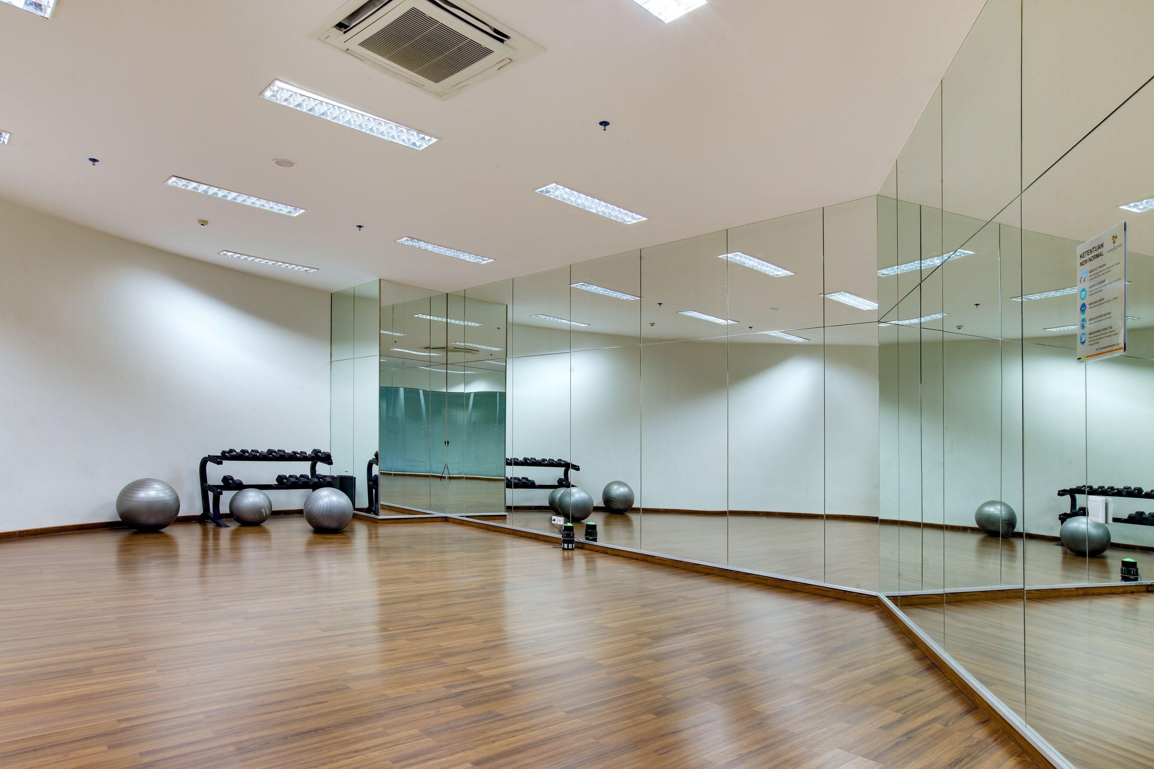 Una habitación amplia con suelo de madera, un espejo grande y equipo de ejercicio, incluyendo mancuernas y pelotas de gimnasia.