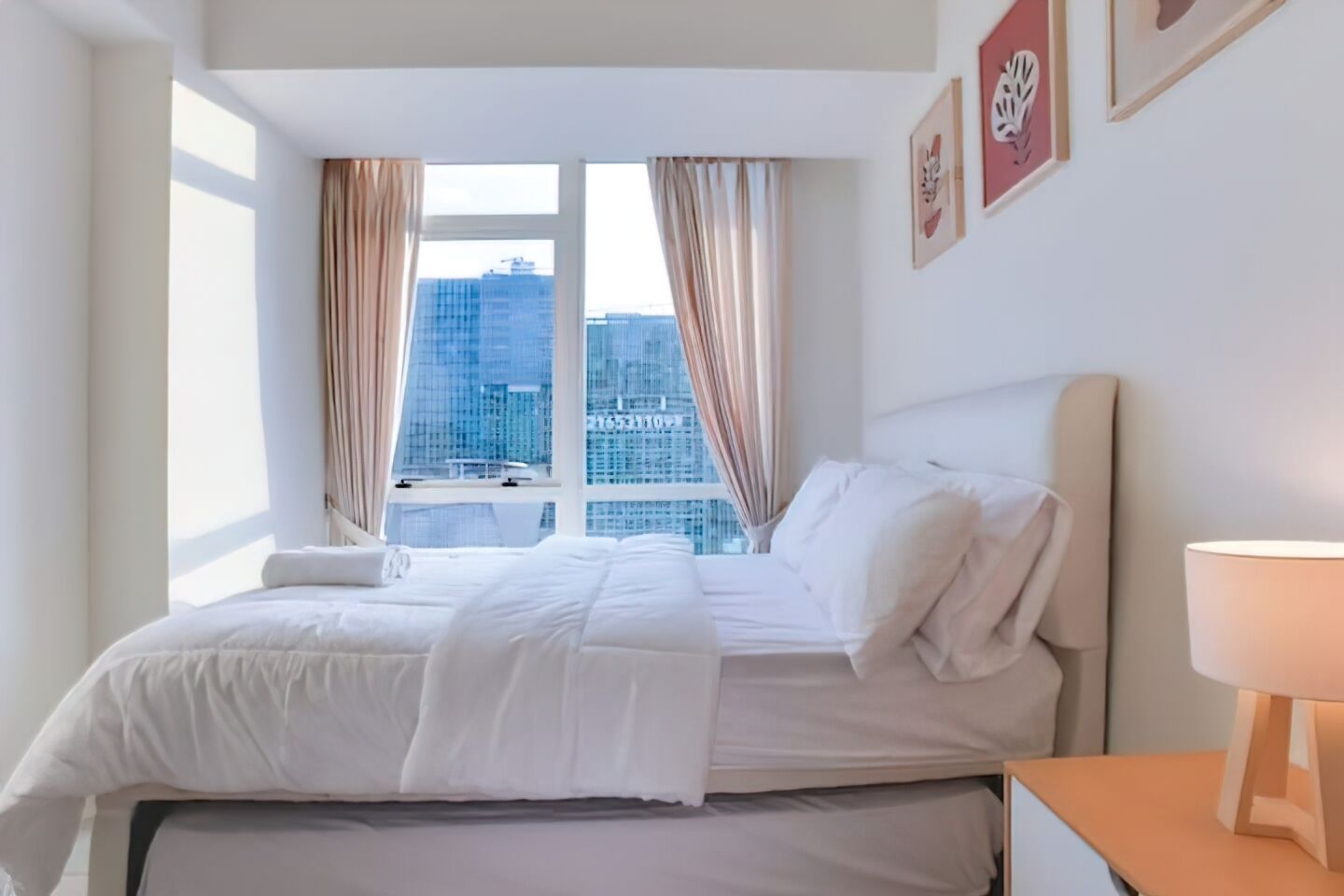 Una habitación de hotel con cama, mesita de noche, lámpara y ventana con cortinas.