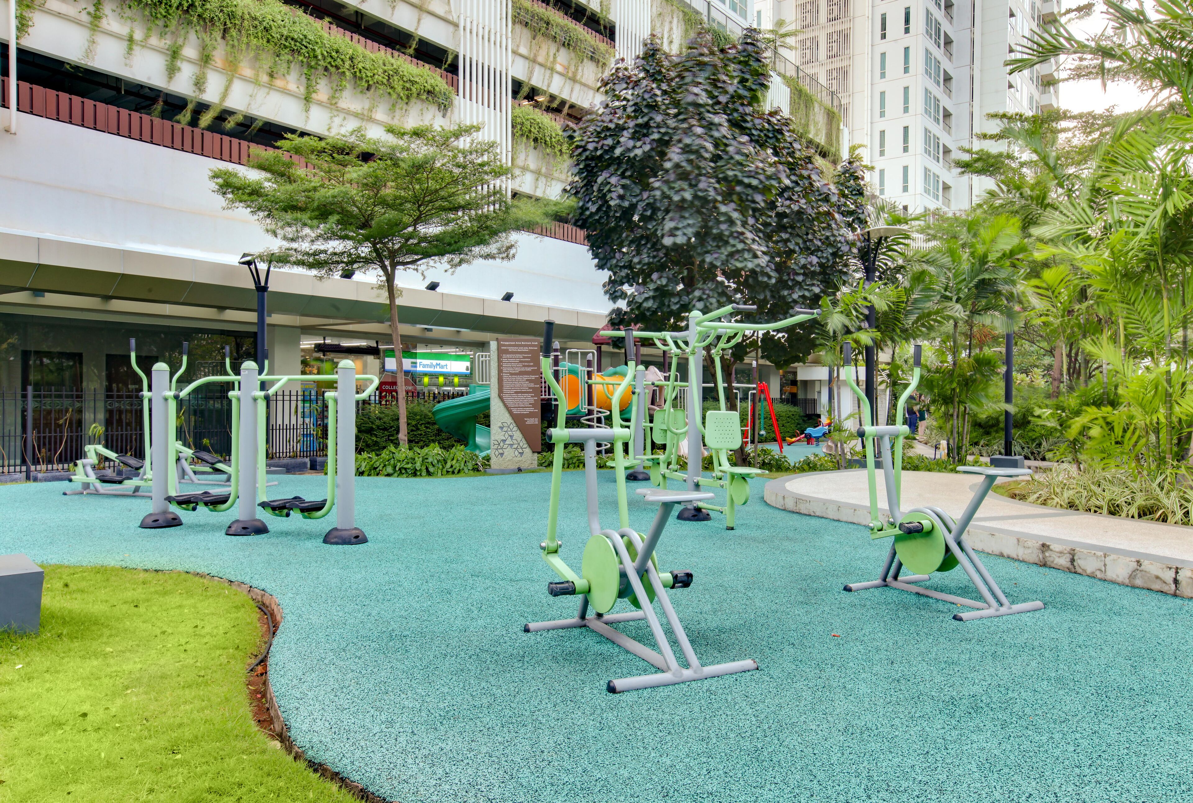 An outdoor gym area with exercise equipment, surrounded by greenery and a building in the background.
