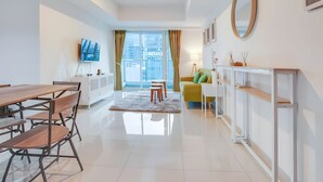 A modern living room with a dining area, a sofa, a TV, and a view of the city. - Staycation Jakarta Kensington Royal (Jakarta)