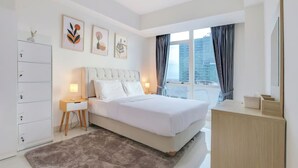A modern hotel room with a large bed, a dresser, a desk, and a window with a city view. - Staycation Jakarta Kensington Royal (Jakarta)