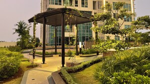 A modern building with a covered outdoor area, surrounded by well-maintained greenery and a pathway. - Staycation Jakarta Kensington Royal (Jakarta)