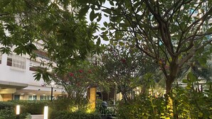 A pathway flanked by lush greenery and illuminated by ground lights, leading to a building with a modern design and a visible entrance. - Staycation Jakarta Kensington Royal (Jakarta)