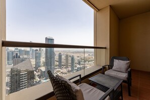 Een balkon met uitzicht op de stad, een rieten stoel, een kleine tafel en hoge gebouwen.