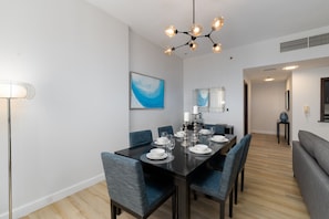 A modern dining area with a black table set for six, blue upholstered chairs, and a contemporary chandelier.